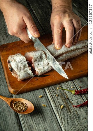 Hands expertly slice a fresh fish on a well-worn wooden board, surrounded by spices and tools in a cozy, rustic kitchen setting. The warm tones create an inviting atmosphere for cooking 123167337