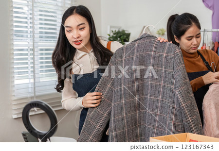 Couple selling clothes online, inspecting stylish plaid jacket and preparing other items in their cozy workspace 123167343
