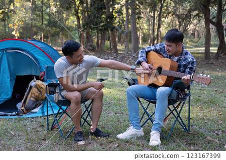 Young Asian homosexual couple camping on a picnic Play guitar together for a relaxing holiday. Young Asian homosexual couple camping on a picnic Play guitar together for a relaxing holiday. 123167399