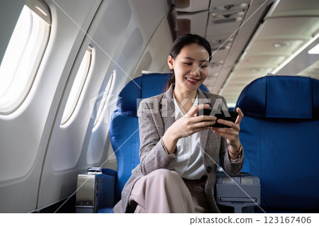Young Asian woman checks business news on mobile phone, sitting near window in first class on airplane during flight, travel and business concept Young Asian woman checks business news on mobile phone, sitting near window in first class on airplane during flight, travel and business concept 123167406