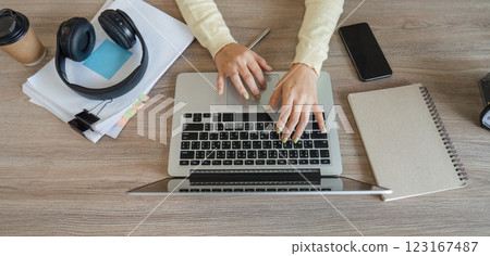 Close-up of hands typing on a laptop in a home office, surrounded by work essentials and personal items. Close-up of hands typing on a laptop in a home office, surrounded by work essentials and personal items. 123167487