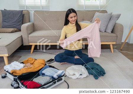Young Woman Packing a Suitcase in a Modern Living Room, Preparing for Travel or Vacation, Organizing Clothes and Essentials Young Woman Packing a Suitcase in a Modern Living Room, Preparing for Travel or Vacation, Organizing Clothes and Essentials 123167490