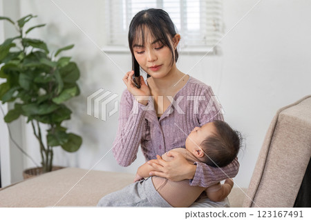 Busy mother multitasking on a phone call while nurturing her baby at home Busy mother multitasking on a phone call while nurturing her baby at home 123167491