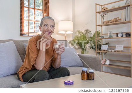 Elderly woman Taking Medicine with a Glass of Water in a Cozy Home Setting for Health and Wellness Concept 123167566