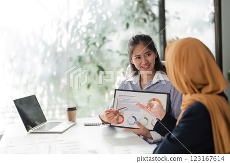 Female finance workers presenting financial data and discussing reports in an office. Female finance workers presenting financial data and discussing reports in an office. 123167614
