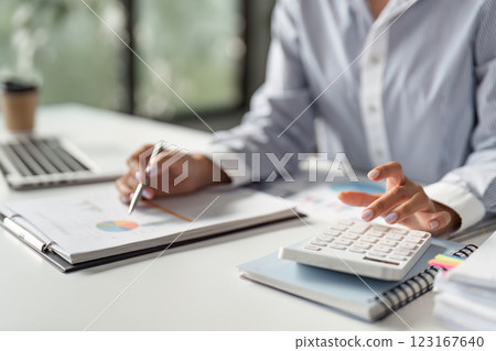 Finance worker calculating data with a calculator and reviewing reports in a modern office. 123167640