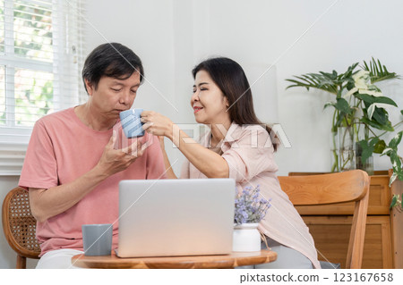 Mature couple sharing a drink while working together on a laptop at home. 123167658