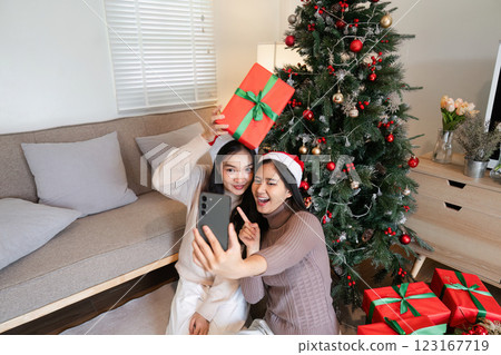 Joyful Young Female Couple Capturing Memories at a Festive Christmas Party with Gifts and Decorations Joyful Young Female Couple Capturing Memories at a Festive Christmas Party with Gifts and Decorations 123167719