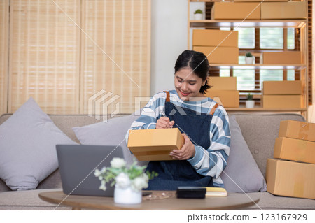 young female entrepreneur writes on the front of a product box to sell products online and prepares to send them to customers. Online selling at home, working from home 123167929