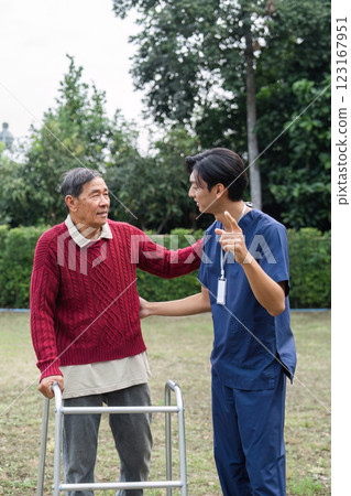 Supportive caregiver sharing a moment with elderly man using walker, fostering connection and well-being in a vibrant garden 123167951