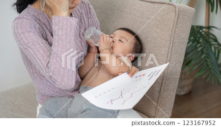 Busy mother contemplating while feeding her baby and reviewing charts in a home office 123167952