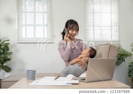 Joyful mother engaging on a phone call while holding her baby at home Joyful mother engaging on a phone call while holding her baby at home 123167986