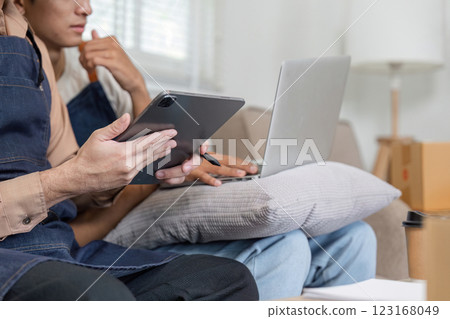 Couple reviewing plans on a tablet and laptop while seated comfortably in their modern living room 123168049
