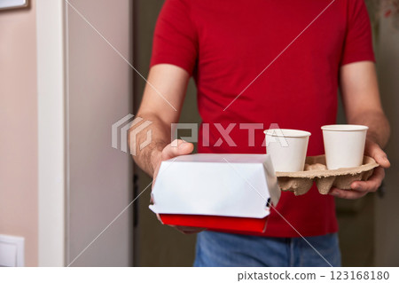 delivery man in red uniform giving food box and paper coffee cups to customer at his front door 123168180