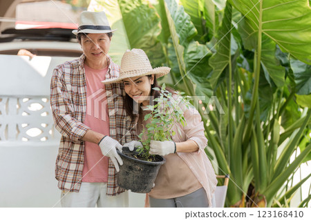 Elderly Asian couple proudly holding a potted herb in their lush garden. 123168410