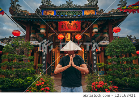 male tourist in a Vietnamese Non La hat prays at temple on a Buddhist pagoda in Hoi An in Vietnam in Asia 123168421