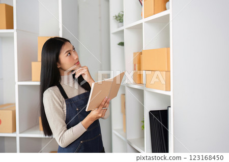 E-commerce businesswoman contemplating inventory while holding a notebook in a modern office. E-commerce businesswoman contemplating inventory while holding a notebook in a modern office. 123168450