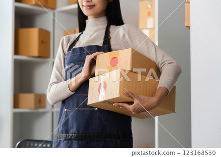 E-commerce businesswoman holding stacked packages with shipping labels in a modern office setting. 123168530