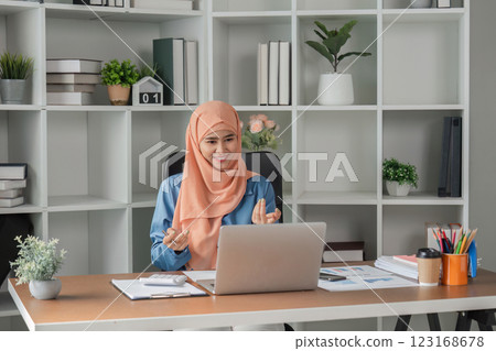 Muslim woman happily discussing in video call while working on a laptop at her desk. 123168678