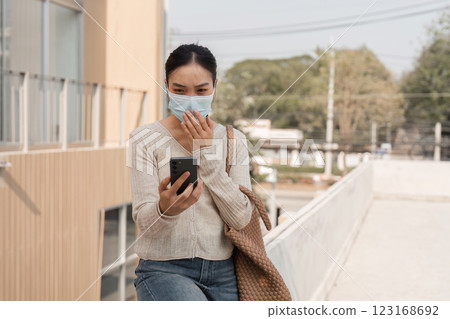 Diverse woman wearing a mask while surprised by smartphone notification outdoors. 123168692