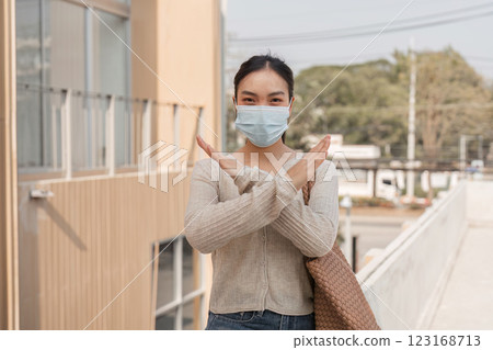 Diverse woman in a mask making a stop gesture outdoors in an urban environment. 123168713