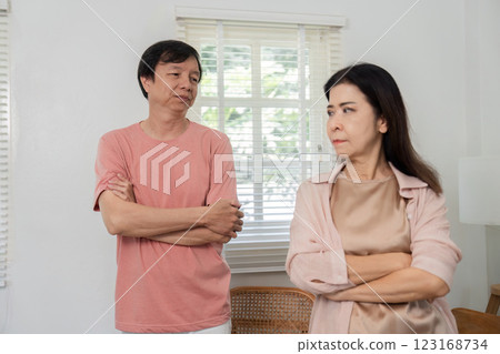 Middle-aged couple standing apart with crossed arms, showing tension indoors. 123168734