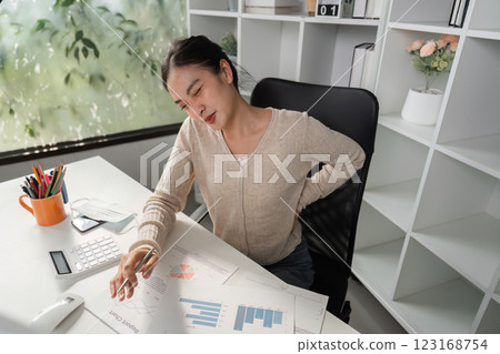 Woman with back pain at desk while analyzing financial charts and graphs. 123168754