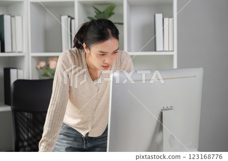Woman leaning on desk while working intently on a computer in an office environment. Woman leaning on desk while working intently on a computer in an office environment. 123168776