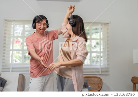 Happy older couple dancing together with headphones in their living room. Happy older couple dancing together with headphones in their living room. 123168780