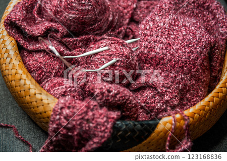 yarns, knitting needles and pattern sample in basket on sofa. 123168836