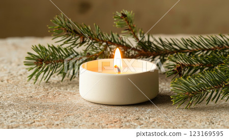 Thin Modern White Candle with Soft Flickering Flame on Rustic Surface Next to Pine Branches. Concept of Christmas, Serenity, Cozy Atmosphere, Winter Decor, Tranquility 123169595