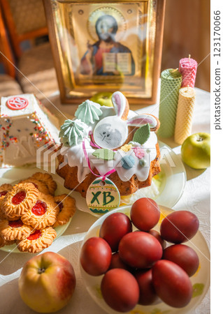 Easter cake with painted eggs, apples and cookies on table in home kitchen. Church icons and candle on background. Orthodox religion theme. Easter cake with painted eggs, apples and cookies on table in home kitchen. Church icons and candle on background. Orthodox religion theme. 123170066