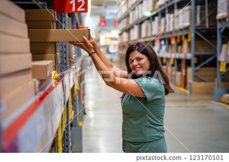 Woman customer looking up and pulling product on shelf while shopping in storage of shop 123170101