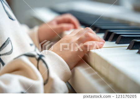Close up view of small hands of girl on white piano synthesizer. Concept of early development: learning music enhances motor skills, hearing, and intelligence, fostering creativity from childhood 123170205