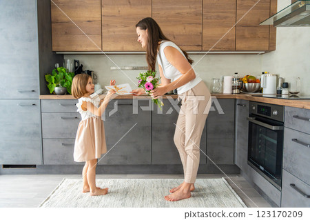 Little girl giving bouquet of flowers and drawing to her mum on the home kitchen. Mothers day, birthday or International Women's Day 8 march concept 123170209