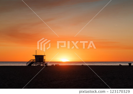 Los Angeles beach at sunset, featuring a lifeguard tower silhouette against a glowing orange and purple horizon 123170329