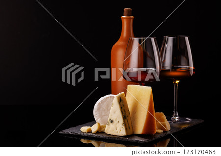 A refined selection of aged cheeses presented on a board, accompanied by a glasses of wine A refined selection of aged cheeses presented on a board, accompanied by a glasses of wine 123170463