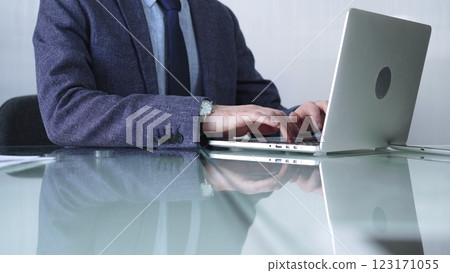 Businessman in blue jacket is focused on typing on laptop at glass desk in modern office, showcasing productivity and concentration, closeup view. Business people concept Businessman in blue jacket is focused on typing on laptop at glass desk in modern office, showcasing productivity and concentration, closeup view. Business people concept 123171055