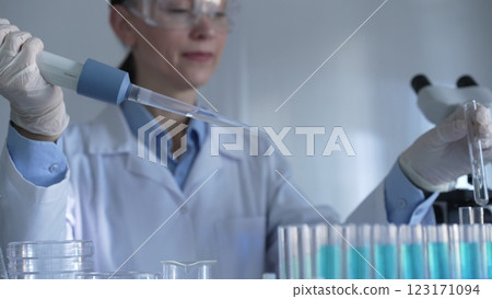 A scientist woman, wearing white gloves and safety glasses, is using a micropipette to drop a liquid into a test tubes. Medicine and science concept A scientist woman, wearing white gloves and safety glasses, is using a micropipette to drop a liquid into a test tubes. Medicine and science concept 123171094