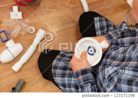 Person assembles plumbing fixtures while sitting on a wooden floor in a home renovation project 123171198