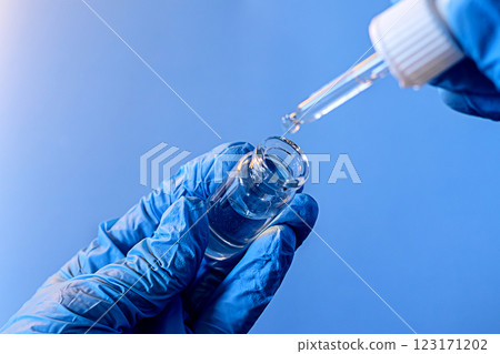 Dropping liquid from a pipette into a glass vial while wearing blue gloves in a laboratory setting 123171202
