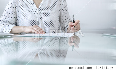 Businesswoman in white dotted blouse is signing a contract at a sleek glass desk in a modern office, showcasing professionalism and focus in her work environment. Business people concept Businesswoman in white dotted blouse is signing a contract at a sleek glass desk in a modern office, showcasing professionalism and focus in her work environment. Business people concept 123171226