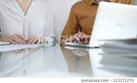 Two unknown accountants are discussing a tax audit, using a laptop and reviewing documents at a glass table, closeup view. Taxes, audit in business Two unknown accountants are discussing a tax audit, using a laptop and reviewing documents at a glass table, closeup view. Taxes, audit in business 123171270