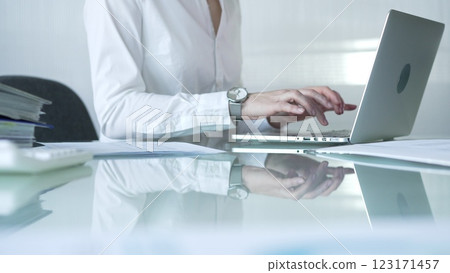 Businesswoman in white blouse typing on laptop at glass desk while sitting in bright office, showcasing productivity and modern work environment. Businesspeople concept Businesswoman in white blouse typing on laptop at glass desk while sitting in bright office, showcasing productivity and modern work environment. Businesspeople concept 123171457
