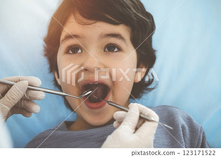 Cute arab boy sitting at dental chair with open mouth during oral checking up with doctor. Visiting sunny dentist office Cute arab boy sitting at dental chair with open mouth during oral checking up with doctor. Visiting sunny dentist office 123171522