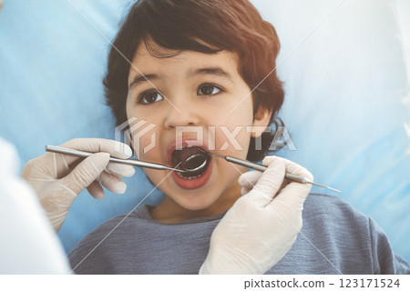 Cute arab boy sitting at dental chair with open mouth during oral checking up with doctor. Visiting sunny dentist office Cute arab boy sitting at dental chair with open mouth during oral checking up with doctor. Visiting sunny dentist office 123171524