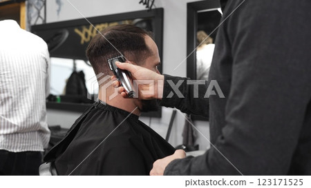 Skilled barber trimming client's hair using electric razor, creating contemporary hairstyle in modern barbershop setting with precise, professional technique 123171525