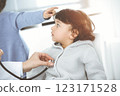 Doctor-woman examining a child patient by stethoscope in sunny clinik. Cute arab boy and his brother at physician appointment 123171528
