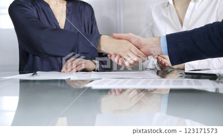 Unrecognizable business partners shaking hands after signing contract at glass table in office meeting, making a deal and closing agreement, close up of handshake Unrecognizable business partners shaking hands after signing contract at glass table in office meeting, making a deal and closing agreement, close up of handshake 123171573