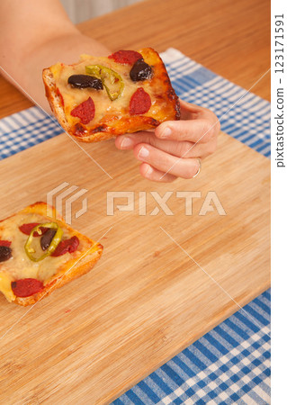Caucasian white person holding pizza pieces on bamboo cutting board on blue napkin Caucasian white person holding pizza pieces on bamboo cutting board on blue napkin 123171591